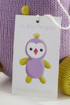 A product tag on a knitted toy reads Icy the Penguin with an illustration of a purple and yellow penguin and the website thejoobles.com below.