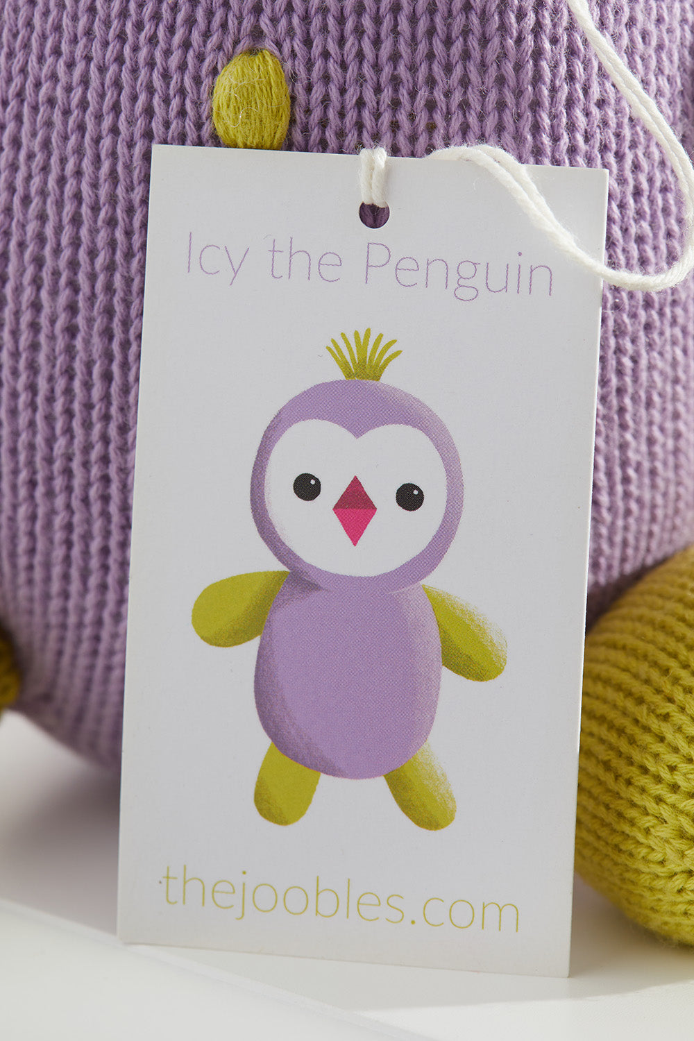 A product tag on a knitted toy reads Icy the Penguin with an illustration of a purple and yellow penguin and the website thejoobles.com below.