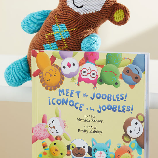 A knitted toy monkey leans against a colorful childrens book titled Meet the Joobles! featuring illustrated animal characters on the cover.