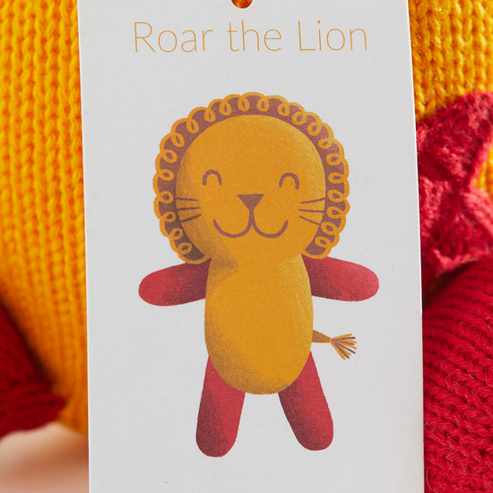A product tag with an illustration of a smiling lion named Roar the Lion and thejoobles.com printed at the bottom, attached to a yellow and red knitted item.